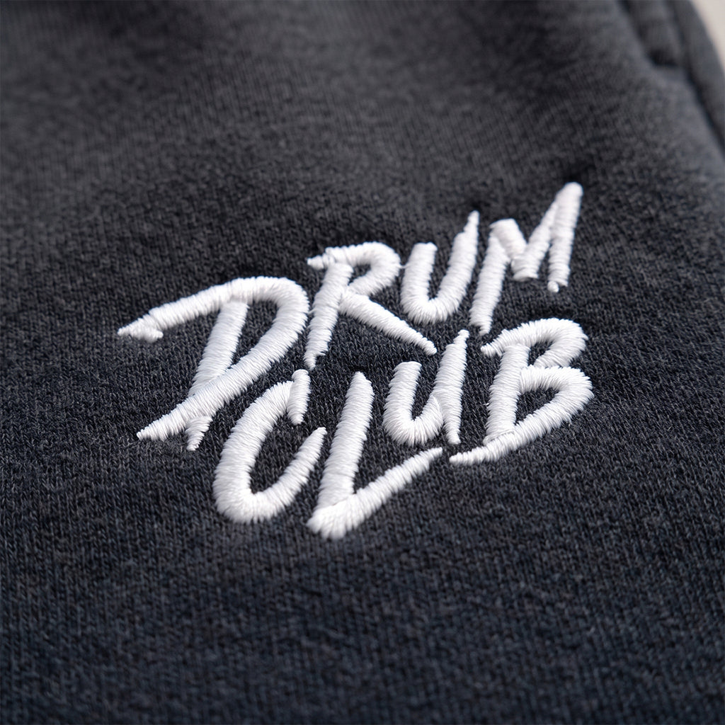Close-up of a dark charcoal gray fabric with white embroidered text reading 'DRUM CLUB'.
