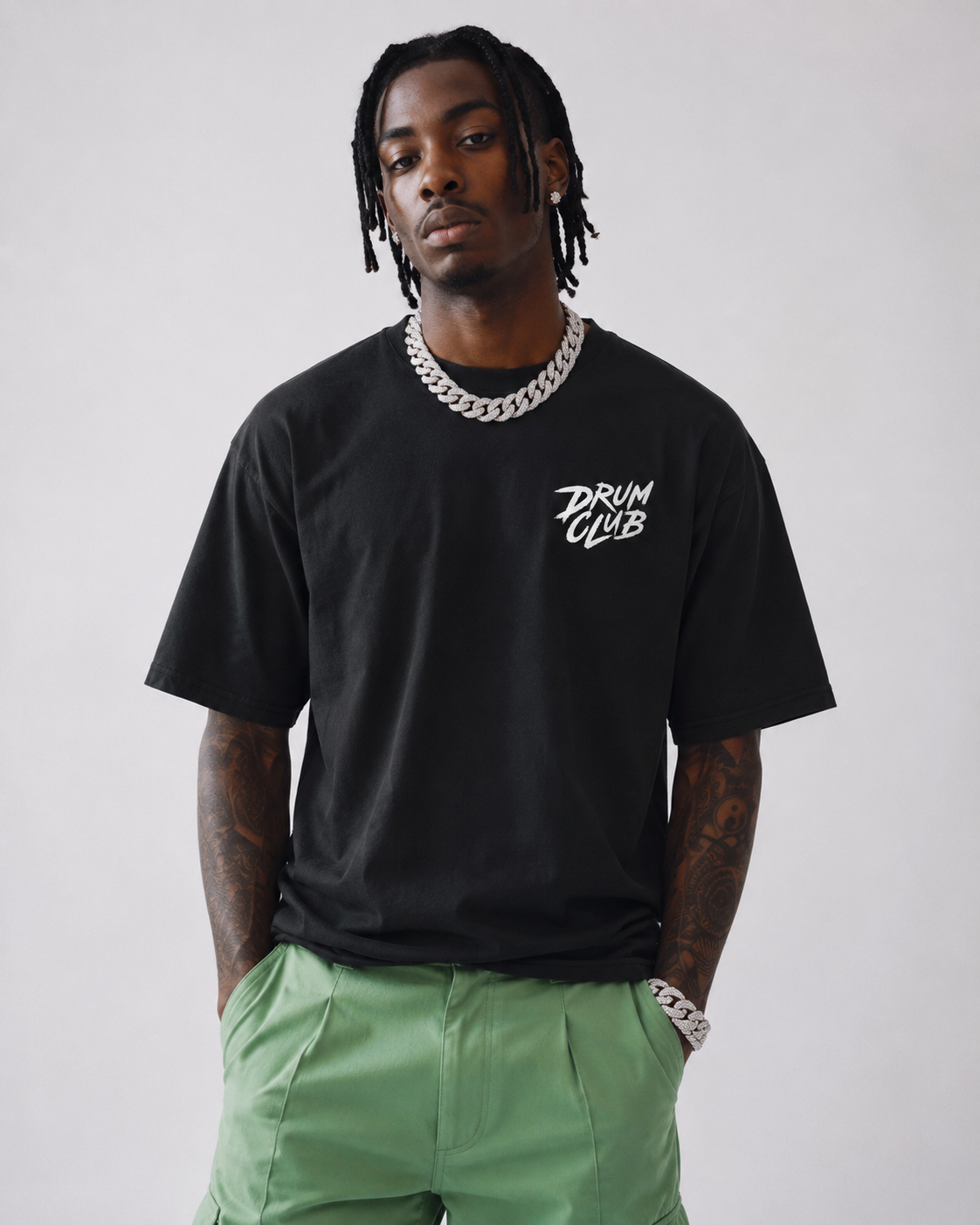Person wearing a black t-shirt with 'Drum Club' text and green pants against a plain background