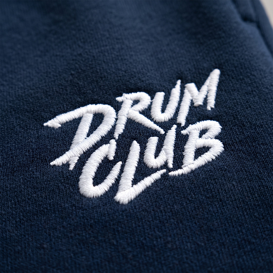 A close-up of a navy blue fabric item featuring white embroidered text that reads 'DRUM CLUB'.
